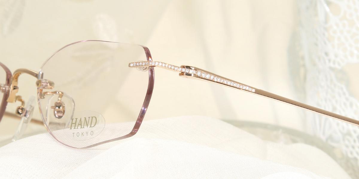 SAKIGAGE玫瑰金鑲鑽女性無框眼鏡置於柔和布料上的近距離側面特寫，展現纖細鏡腳與閃耀鑽石細節